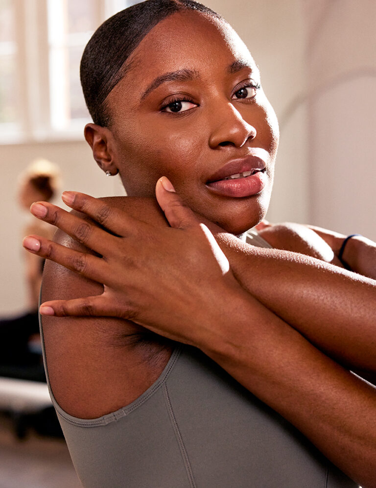 A woman in a grey top looking at the camera as she stretches her arm