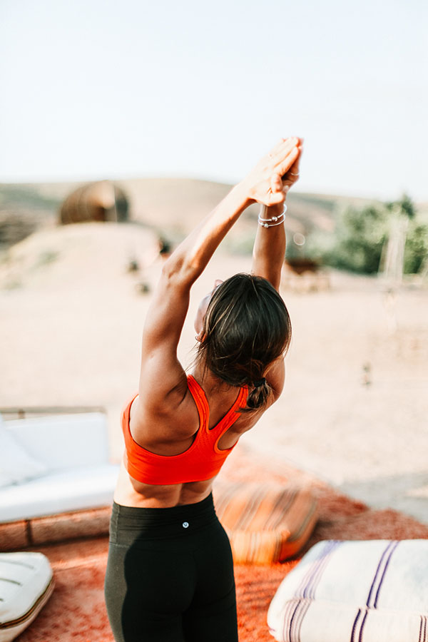 A woman in red and black gym clothes stretching with her arms up in the air