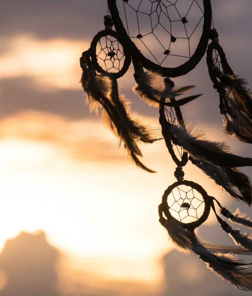 A dreamcatcher swaying in the wind in front of a sunset