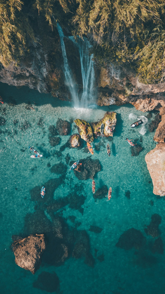 A view from above of a lagoon with paddle boarders and a waterfall