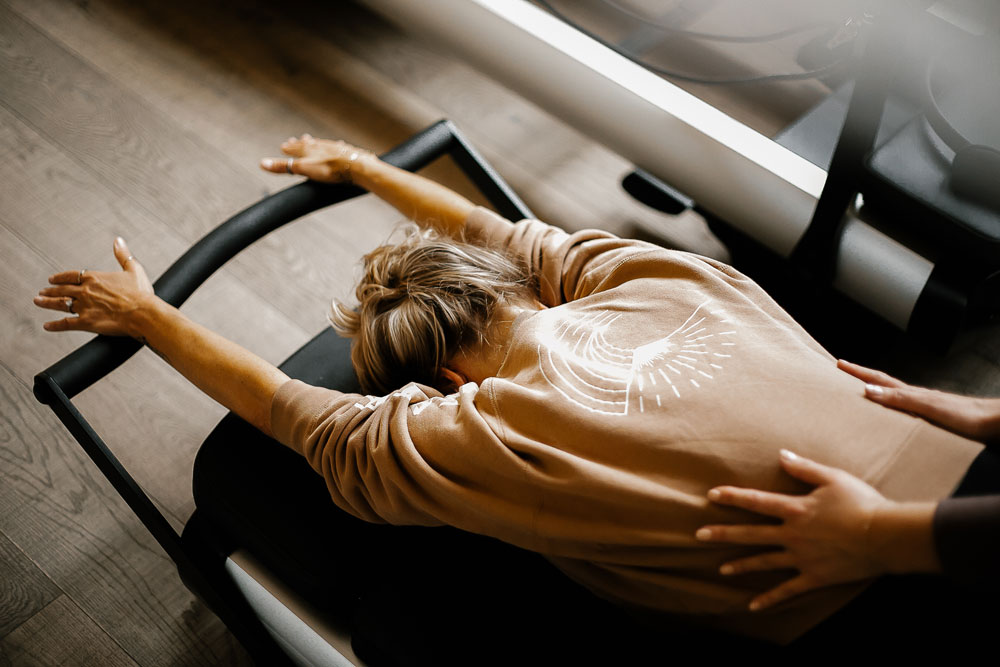 Woman is face down on a pilates machine with hands on her lower back