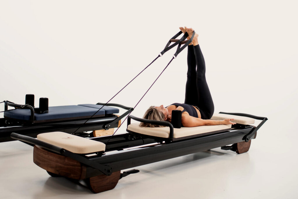 woman lies on reformer with feet in the air