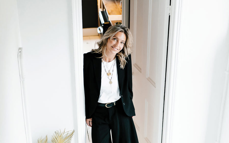 Blonde woman in black blazer smiles and looks up into camera